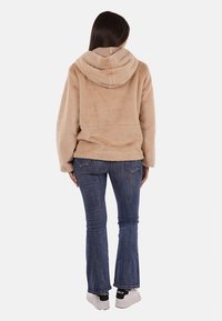 Felpa con cappuccio in pelliccia sintetica beige, vestibilità morbida e texture liscia. Abbinata a jeans blu a gamba stretta e sneakers.