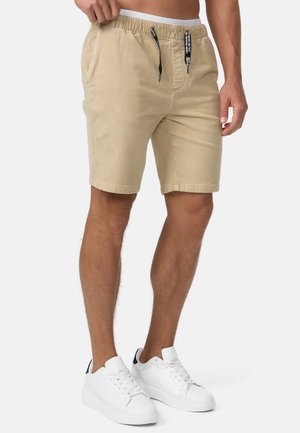 Shorts en velours côtelé beige avec une taille élastique, un cordon de serrage et des poches latérales. Assortis à des baskets blanches.