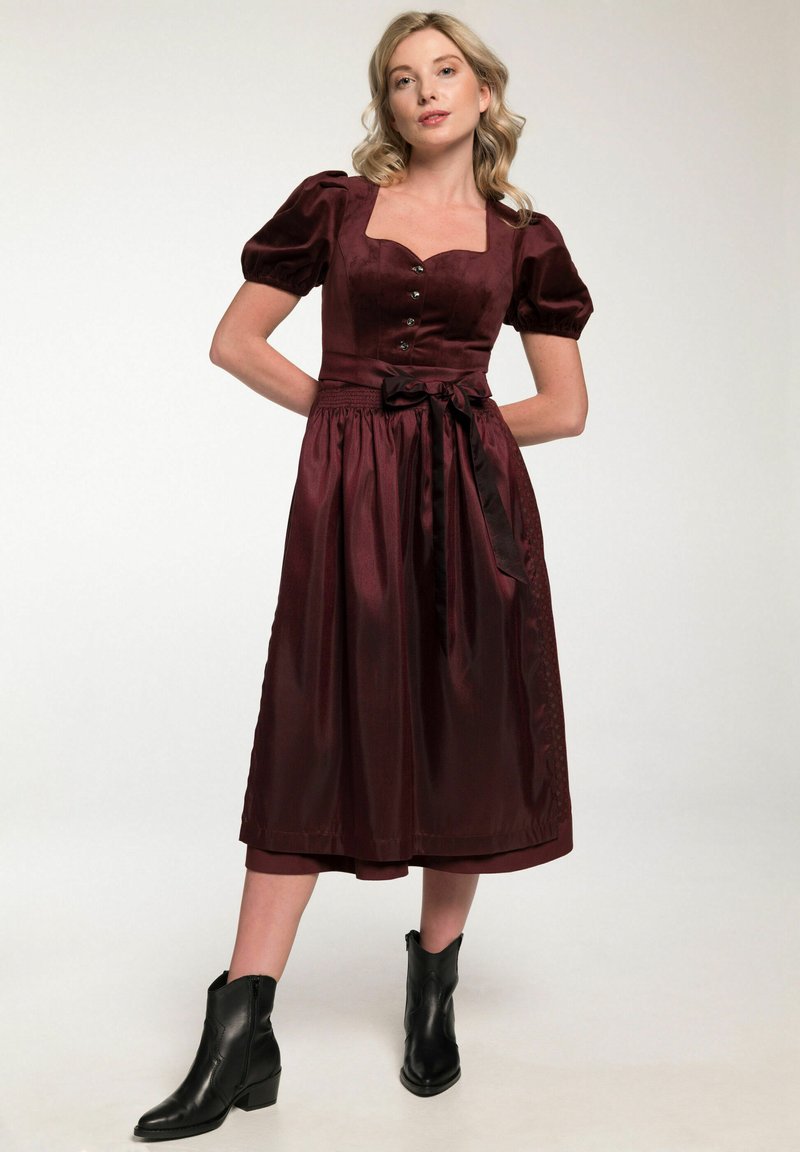 Bordeauxrotes Kleid mit Puffärmeln, quadratischem Ausschnitt, Knopfdetails und gebundenem Taillenband. Kombiniert mit schwarzen Knöchelstiefeln. Glatte Textur.
