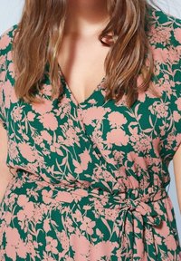 Vestido envolvente floral en verde oscuro con flores rosas. Presenta un escote en V, manga corta y una cintura atada para un ajuste ajustable. Tejido suave.