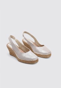 Zapatos de cuña con tiras traseras en color plateado, con un acabado de brillo texturizado y suelas de yute natural trenzado. Puntera redondeada y detalles cosidos a lo largo de los bordes.