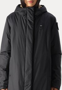 Schwarzer isolierter Mantel mit hohem Kragen, Frontreißverschluss, zweiseitlichen Taschen und einem weichen Innenfutter. Verfügt über ein Markenetikett auf der Brust.