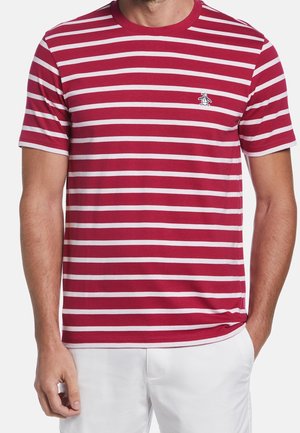 Uomo che indossa una maglietta a maniche corte a righe orizzontali rosse e bianche con un piccolo logo di pinguino sul petto, abbinata a pantaloni bianchi.