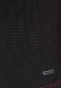 Tela negra con un patrón de cuadrícula, con una etiqueta ProW-B y acentos de costura roja. La textura parece suave y duradera.