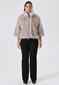 Kunstpelzjacke in hellem Beige mit flauschiger Textur und weitem Kragen, kombiniert mit schwarzen, taillierten Hosen und spitzen schwarzen Schuhen.