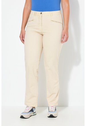 Pantaloni in cotone beige con una vestibilità a gamba dritta, dotati di tasche frontali e chiusura con zip, abbinati a scarpe da ginnastica grigie e blu.