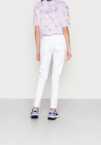 Jeans ajustados blancos con detalles en los bolsillos traseros, combinados con una camiseta de manga corta en tie-dye lavanda y zapatillas moradas con acentos negros.