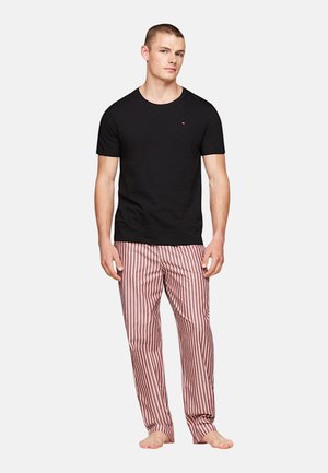 T-shirt nera in cotone a maniche corte abbinata a pantaloni del pigiama a righe rosse e bianche, con un fit dritto e un design rilassato.