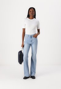 Jeans svasati azzurri chiari con vita alta, abbinati a una t-shirt bianca attillata a maniche corte. Una borsa nera e scarpe completano il look.