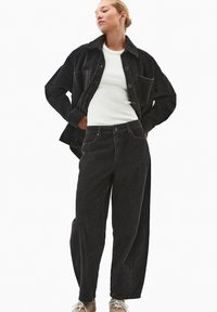 Sort fløjlskajot med en lomme, parret med matchende fløjlshandsker. Hvid tætsiddende T-shirt under. Neutralt fodtøj fuldender looket.