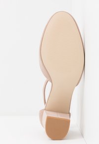 Vue de la semelle d'une sandale à talon en daim beige avec une fine bride et une pointe de talon en caoutchouc texturé sur fond blanc.