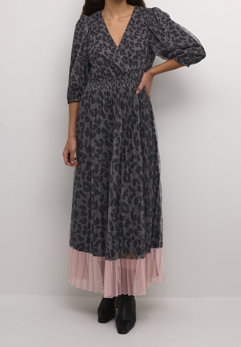 Šedé šaty s leopardím potiskem, s nabíranými rukávy, výstřihem do V a řaseným růžovým lemem, vyrobené z lehkého materiálu, doplněné černými kotníkovými botami.