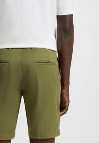 Olive green shorts made of a lightweight fabric, featuring a flat front, two back pockets, and visible stitching along the hem.