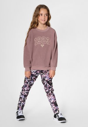 Lila fleecetröja med "1923" broderat i guld, ihop med multicolor kamouflagemönstrade leggings och svarta sneakers med vita snören.