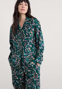 Floralni pidžama set s tirkiznom podlogom i raznobojnim uzorcima cvijeća i školjki. Izrađen od mekanog materijala s opuštenim krojem i džepovima.
