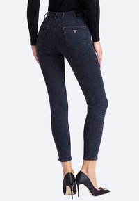 Jeans ajustados negros con una cintura de altura media, textura de denim suave y bolsillos traseros estándar que presentan un pequeño acento de logo plateado.