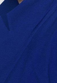 Tejido azul real con una textura suave, que presenta un diseño de cuello afilado y angular, y detalles de costura limpios. El borde está ligeramente elevado.