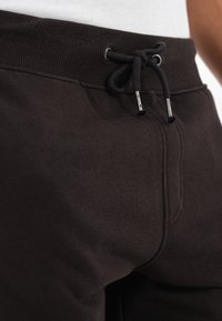 Pantaloni comodi neri con un elastico a costine in vita, cordoncino con estremità in metallo e una texture di tessuto morbida. I dettagli includono cuciture frontali e tasche.