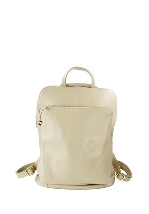 Sac à dos en cuir beige avec poche avant zippée, poignée supérieure, bretelles réglables, et petite étiquette aux rayures rouges, blanches et vertes.