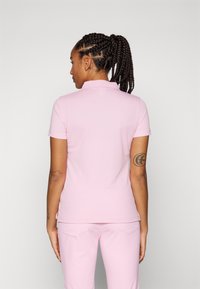 Camisa polo rosa de mangas curtas e acabamento texturizado, com colarinho e pequeno detalhe de logo na parte traseira. Combinada com calças a condizer.