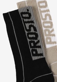 Czarne i beżowe skarpetki o prążkowanej fakturze, z dzianymi logo marki w kontrastujących kolorach oraz subtelnymi paskami.