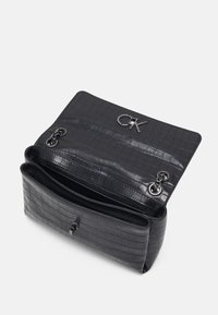 Czarna torebka z tłoczeniem imitującym skórę krokodyla, z srebrnym logo, klapką zamykającą, dwoma przegródkami oraz ozdobnymi elementami metalowymi.