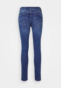Jeans ajustados de mezclilla azul oscuro, con una cintura de altura media, dos bolsillos traseros con costura curva y un acabado suave, ligeramente texturizado.