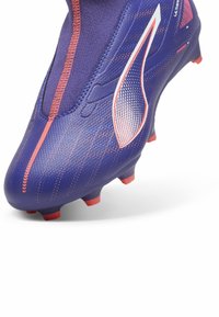 Scarpina da calcio viola con tomaia sintetica testurizzata, caratterizzata da dettagli arancioni e un design bianco. Dotata di tacchetti rossi stampati per un'ottima trazione.