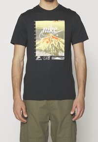 Svart bomullströja med en grafisk design av en vulkan och "Nike"-text, korta ärmar och rundad halsringning.