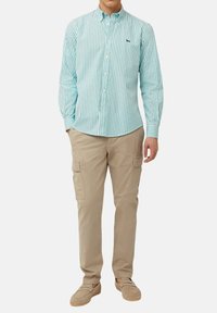 Lichtblauw en wit gestreepte button-up shirt, khaki cargo broek en tan instap schoenen. Het shirt heeft een klein marineblauw logo.