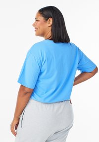 Lyseblå top med korte ærmer og løs pasform, kombineret med grå joggebukser. Glat stof med et enkelt, afslappet design.