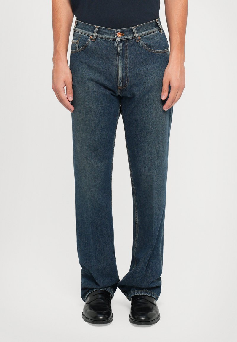 Blå denimjeans med rak passform, femficksdesign, kontrasterande sömmar och knäppning fram. Bärs med svarta skor.