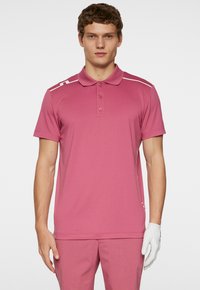 Kortärmad rosa polo med krage, med vita ränder på axlarna, tillverkad av texturerad tyg. Bärs med matchande byxor och en handske.