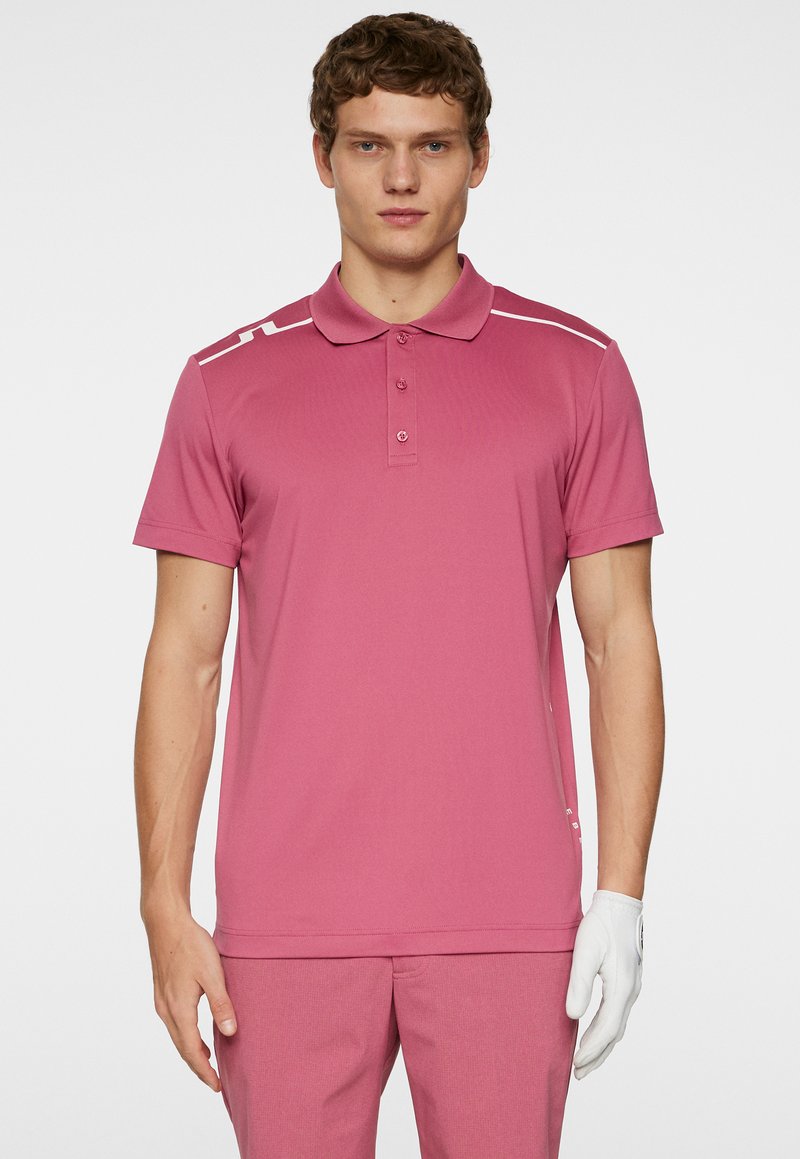 Kortärmad rosa polo med krage, med vita ränder på axlarna, tillverkad av texturerad tyg. Bärs med matchande byxor och en handske.