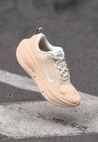 Beige Nike Zoom sneakers met een textuur van mesh bovenkant, witte swoosh en een gebogen zoolontwerp. Bevat veters en een trekhaak op de hiel.