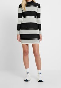 Abito a righe nero e grigio, con coste, maniche lunghe e collo alto, caratterizzato da strisce bianche di accento. Indossato con sneakers bianche.