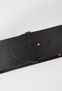 Black leather belt with a rounded end, secure loop for adjustment, and gold hardware accent with multiple sizing holes. Smooth texture.
