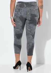 Jeggings grises con estampado, que presentan diseños de paisley y acentos con tachuelas, con un corte cropped y una silueta entallada. Vista posterior mostrada.