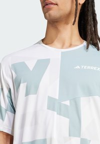 Short-sleeve white athletic shirt with geometric light blue patterns, a crew neck, and "TERREX" logo at the chest. Smooth texture.