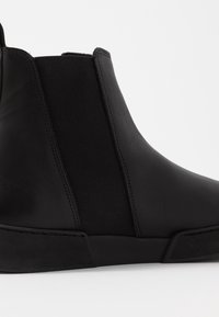 Černé kotníkové boty z hladké kůže s elastickými bočními panely. Elegantní, zaoblený design, texturovaná gumová podrážka. Bez viditelných kovových částí nebo vzorů.