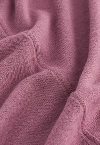 Miękka, teksturowana tkanina w stonowanym odcieniu lawendy, z prążkowanym brzegiem i subtelnym wzorem dzianiny, tworząca przytulny wygląd.