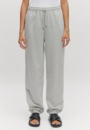 Lichtgrijze sweatpants met een trekkoord in de taille, brede pijpen en elastische boorden, gecombineerd met zwarte slidesandalen. Zachte textuur, casual ontwerp.