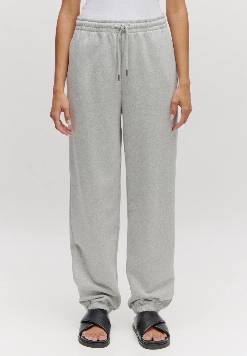 Helle graue Sweatpants mit einem Kordelzugbund, weiten Beinen und elastischen Bündchen, kombiniert mit schwarzen Slipper-Sandalen. Weiche Textur, lässiges Design.