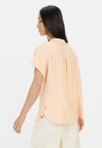 Korte mouwen shirt in pastel oranje met witte verticale strepen, met een ronde onderkant, een relaxed fit en een klein logo-detail op de achterkant.
