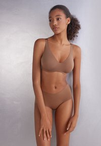 Hnědá bezšvová souprava spodního prádla vyrobená z měkké, elastické tkaniny. Podprsenka má široké ramínka a design ve tvaru V; kalhotky jsou středně vysoké.