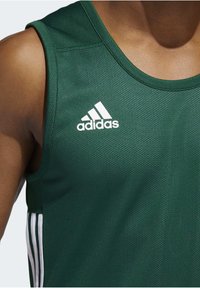 Grünes sportliches Tanktop aus strukturiertem Mesh-Stoff. Verfügt über das weiße Adidas-Logo und gestreifte Akzente an den Seiten. Rundhals-Design.