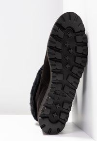 Bota de ante negra con una suela de goma negra texturizada que presenta surcos profundos para un buen agarre, complementada con un borde de piel de pelo en el tobillo. Talla 37.