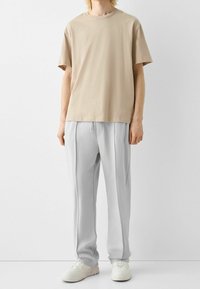 Beige bomulls-t-shirt med korta ärmar, kombinerad med ljusgrå sweatpants med dragsko i midjan och sidoseams. Vita sneakers fullbordar looken.