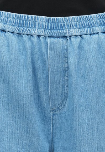 Gaiši zili džinsu bikses ar elastīgu jostu un savilktu audumu jostasvietā. Iespējas iekļauj priekšējo kabatu un mīkstu tekstūru.