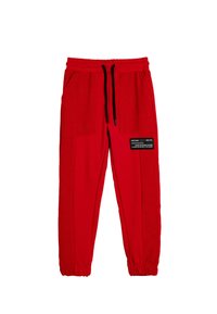 Rote Sweatpants aus weichem Stoff, mit elastischem Bund, Kordelzugverschluss und zwei seitlichen Taschen. Schwarzes Akzentpatch auf dem Bein.